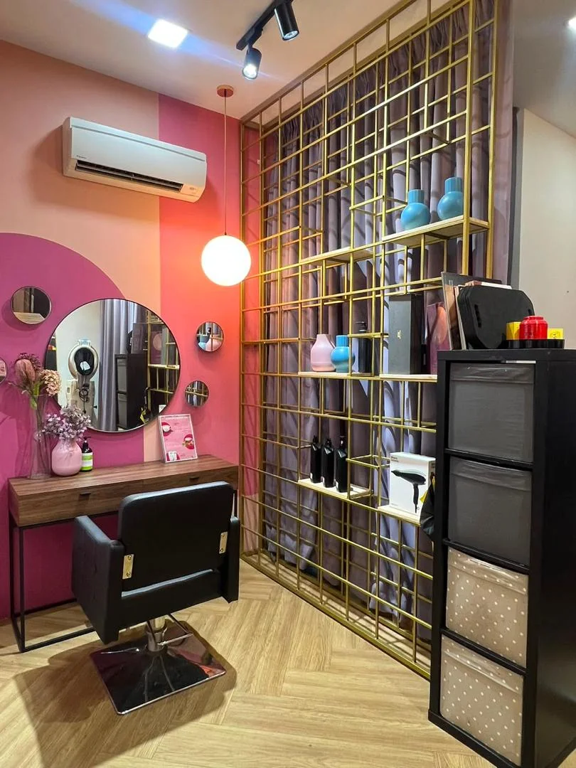 Styling station at Dashing Diva Plaza Damas with a round mirror, pendant lamp and gold shelving
